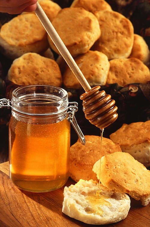 A jar of honey with a dipper and a biscuit 