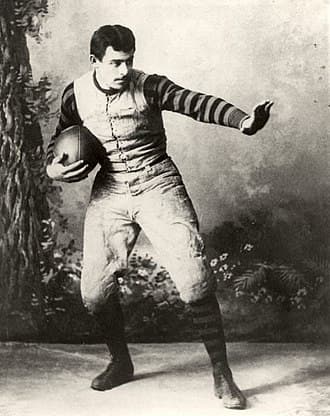 John Heisman, a University of Pennsylvania Law School class of 1892 alumnus and rugby football player, posing at Penn in 1891 holding an elongated ellipsoidal rugby ball and gestures resembling the famed "Heisman Pose" associated with the Heisman Trophy, named in his honor[32]